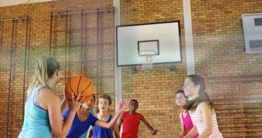 Basketbol topu tutan, deniz mavisi atlet. Spor salonunda basket potası ve fotokopi alanıyla geçmeye hazırlanıyor. Takım çalışması, atletizm, gençlik, rekabet, eğitim, fitness, kentsel