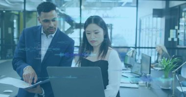 İş kıyafetleri içinde işbirliği yapan profesyoneller açık planlı ofisteki doküman ve laptopları işaret ediyorlar. İş, takım çalışması, modern, çalışma alanı, teknoloji, işbirliği, şirket