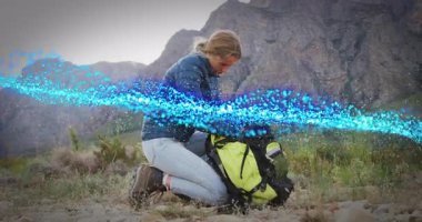 Hiker kneeling on mountain unzipping neon pack creating animated blue particles on screen tech demo. Adventure, exploration, wilderness, technology, nature, innovation, outdoor