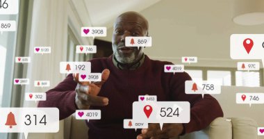 Burgundy süveterli bir adam oturma odasındaki izleyiciye uyarı simgeleriyle işaret ediyor. Modern, oturma odası, dijital, iletişim, rahatlama, teknoloji, konfor