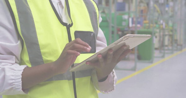 Using tablet smartphone, technician wearing safety vest inspecting factory floor, copy space. Industrial, technology, industrialwear, enterprise, modern, safety, equipment