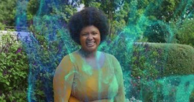 Bahçede gülümseyen orta yaşlı bir kadın teknolojik gösteride gövde etrafında dönen turkuaz enerji ağını aktifleştiriyor. Kadınlık, canlılık, dijital, yenilik, doğal, uyum, dinamik