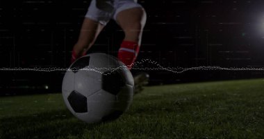 Sahada stadyum ışığı altında yuvarlanan futbol topu, kramponlu oyuncu tekme atıyor, dalga boyu üst üste biniyor. Atletik, hareketli, dijital, teknoloji, spor, performans, canlı