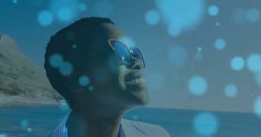 Kedi gözlü güneş gözlüklü, çizgili tişörtlü, fotokopi çekilen sahile bakan gülümseyen kadın. Macera, eğlence, moda, sükunet, doğa, zarafet, rahatlama