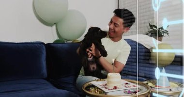 Evcil hayvan kutlaması, bir adamın yavru köpeği kaldırmasını, pastaya mum üflemesini animasyon konfetiyle yönlendirmesini gösteriyor. Neşe, arkadaşlık, neşeli, neşeli, samimi, şefkatli, boş zaman