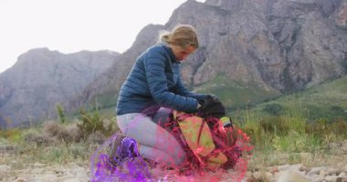 Female hiker kneeling meadow unzipping backpack and revealing swirling purple energy in tech demo. Adventure, empowerment, exploration, outdoor, vibrant, mystical, resilience