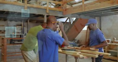 Eğitmen ahşap atölyesine giriyor öğrencilere yol gösteriyor. Tahtaları bant ile ölçüyor ve kesinlik için işaretliyor. İşçilik, çıraklık, işbirliği, sanayi, manuel, beceri geliştirme, atölye