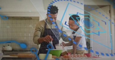 Baba ve oğul yeşil karıştırma kabını yerleştiriyor, yemek pişirme dersi için süt koyuyor ve hamuru çırpıyor. Aileler, kaynaşma, işbirliği, mutfak, aile içi, birliktelik, neşe