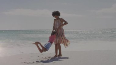 Afrika kökenli Amerikalı kadın ve kızının kumsalda birlikte oynamalarının animasyonu. Yaşam tarzı, aile ve ışık konsepti dijital olarak oluşturulmuş video.
