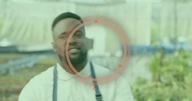 Seranın içindeki kameraya dönen bir adam fidan tepsileri arasında kırmızı HUD tarama yüzünü aktifleştiriyor. Bahçıvanlık, bahçıvanlık, teknoloji, yenilik, sera, büyüme, sürdürülebilirlik