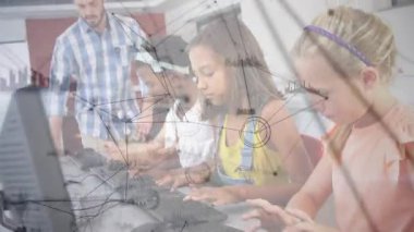 Eğitim laboratuarında daktilo rehberliği yapan öğrencilerin arkasında yürüyen eğitmen. Sınıf, teknoloji, öğrenme, takım çalışması, akıl hocalığı, eğitim, dijital