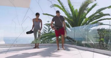 Egzersiz ikilisi deniz manzaralı balkona çıkıyor, su şişelerini yerleştiriyor, spor yapmak için yoga minderlerini açıyor. Egzersiz, sağlık, dinginlik, açık hava, fitness, istikrar, farkındalık.