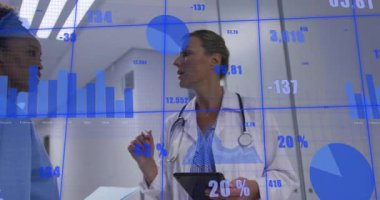 Physician gesturing tablet showing health metrics via 3D charts while nurse moving corridor. Medical, technology, digital, healthcare, professional, futuristic, communication
