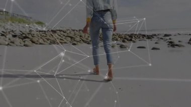 Barefoot woman pressing wet sand and walking shoreline, technology overlay expanding over beach. Serenity, connectivity, coastal, contemporary, exploration, tranquility, digital