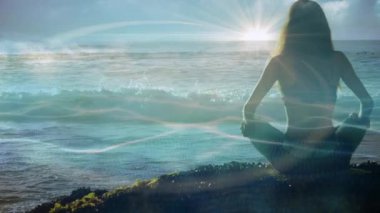 Sahilde oturan bir kadın, güneş ışığı soluyor, kollarını yükselen güneşe doğru kaldırıyor sağlık ayini için. Meditasyon, sükunet, dinginlik, farkındalık, şafak, doğa, rahatlama