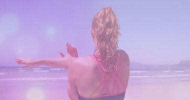 Sahilde yoga yapan beyaz bir kadının arka planda ışık animasyonu. Etkin yaşam tarzı, spor, rahatlama ve deniz konsepti dijital olarak oluşturulmuş video.