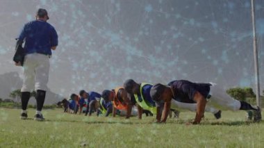 Koç, beysbol takımında şınav çekerek forma bakıyor, kıvılcımlar öne çıkıyor. Atletizm, takım çalışması, antrenman, açık hava, disiplin, motivasyon, sportmenlik