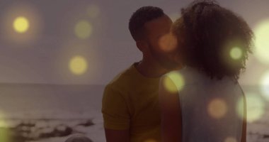 Gün batımında kumlu sahilde oturan öpüşen çift, hafif dalgalar ve hafif alevlerle. Romantizm, samimiyet, günbatımı, dinginlik, doğa, sıcaklık, bağlantı