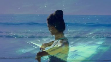 Female starting chest stretching at shoreline causing fitness grid overlay growing over waves. Health, wellness, mindfulness, relaxation, digital, technology, nature