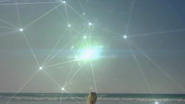 Güneş ışıkları ve dijital ışıldayan kadın teknoloji ağı etrafında gezinirken sahilde ayakta duruyor. Gelecek, sükunet, bağlantı, dinginlik, yenilik, manzara, ilerleme