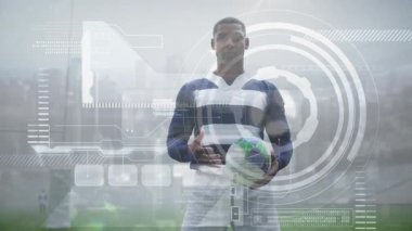 Erkek sporcu ragbi topu tutuşu yapıyor. HUD ile ölçümleri takip ederken duruşu ayarlıyor. Sporcu, stadyum, spor giyim, teknoloji, fitness, performans, eğitim