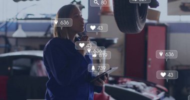 Tamirci, kaputu açık, elinde tablet olan araba tamirhanesinde yükseltilmiş lastiği inceliyor. Otomotiv, endüstri, onarım, teşhis, teknoloji, mühendislik, kesinlik