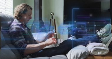 Ekose gömlekli bir adam dizüstü bilgisayarda yazıyor, oturma odasında kredi kartı tutuyor, devre kaplamalı. Teknoloji, uzaktan çalışma, dijital ticaret, modern ev, günlük yaşam tarzı, yenilik, bağlantı