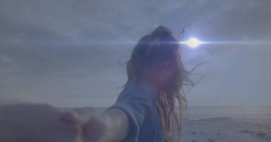 Partnerin elini tutuyor, kot gömlek giyen bir kadın kumlu sahilde yürüyor, güneş parlıyor. Romantizm, bağlantı, macera, dinginlik, rahatlık, doğa, uyum