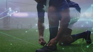 Diz çökmüş futbolcu sahada krampon bağcıklarını sıkıyor, maç hazırlığı için analizleri etkinleştiriyor. Sporcu, spor giyim, modern tasarım, performans, fitness, stadyum, kararlılık