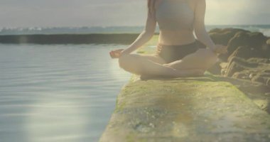 Kumsalda yoga yapan beyaz bir kadının üzerine ışık animasyonu. Etkin yaşam tarzı, spor, rahatlama ve deniz konsepti dijital olarak oluşturulmuş video.