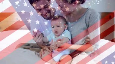 Amerika bayrağı ve konfeti animasyonu mutlu beyaz anne babaların yatak odasında bebekle oynamaları üzerine. aile, ebeveynlik, birliktelik ve vatanseverlik dijital olarak üretilen video konsepti.