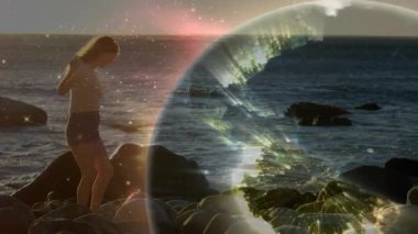 Gün batımı ufku parlayan Dünya küresinin kayalık sahil kadınında dönmesine ve teknolojik demo izlemesine neden oluyor. Doğa, ufuk, dinginlik, teknoloji, gelecekçilik, manzara, yansıma