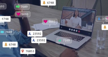 Mavi gömlekli bir adam, elinde dijital simgelerle ofiste doküman tutan meslektaşını dizüstü bilgisayarla izliyor. İşbirliği, iletişim, teknoloji, takım çalışması, profesyonel, üretkenlik, dijital