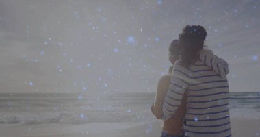 Alacakaranlıkta kumlu sahilde turuncu bluz ve çizgili kapüşonlu kapüşonlu giyen, okyanus dalgalı bir çift. Romantik, dostluk, sükunet, manzara, siluet, bağlantı, sükunet