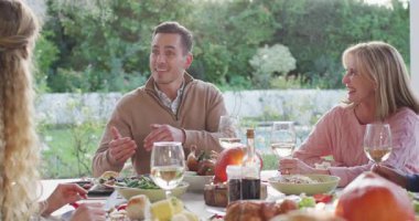 Masanın üstündeki mutfak verandasında ailesiyle anekdotu paylaşan bir adam. Aile, açık hava yemeği, kutlama, neşe, kırsal, birliktelik, rahatlama.