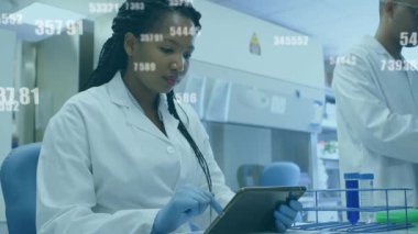 Kadın araştırmacı tıkırtı tableti, laboratuvar verilerini erkek araştırmacı örneklerini hazırlarken üst üste koyuyor. Bilim, yenilik, teknoloji, kesinlik, işbirliği, analitik, modern