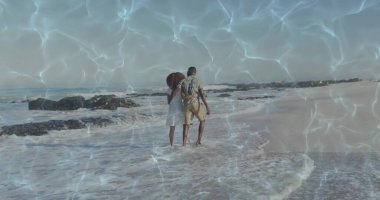 Çıplak ayaklı, kumlu sahilde kol kola yürüyen, sığ su ve kayalık çıkıntıları olan bir çift. Romantizm, çift, deniz kenarı, dinginlik, uyum, eğlence, açık hava