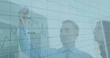 Olgun iş adamı modern ofisteki cam tahtaya çizgi grafikleri çizer ve analiz eder. Şirket, strateji, sunum, analitik, veri görselleştirme, işbirliği, profesyonel