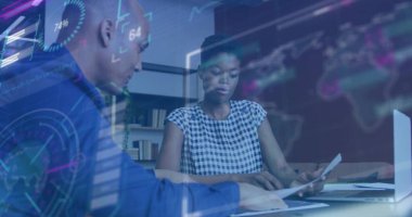 Belgeleri incelemek ve dizüstü bilgisayarda yazmak. Ofis masasında iki iş arkadaşı, holografik çizelgelerle. İşbirliği, analiz, toplantı, çalışma alanı, teknoloji, veri, yenilik