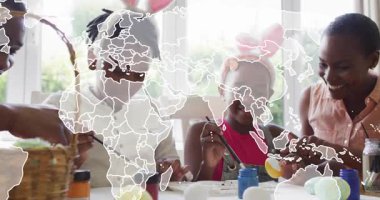 Aile, eğitim için masa etrafında toplanıp yumurta boyuyor ve dünya haritası kıtaları örtüyor. Şenlik, takım çalışması, yaratıcılık, bağlılık, çok kültürlülük, kutlama, sanatsal