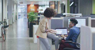 Reviewing documents and using laptops, coworkers wearing blazers working in office, with bicycle. Collaboration, teamwork, modernoffice, productivity, workspace, professional, designstyle