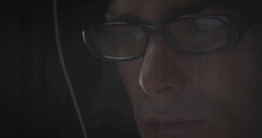 Showing man wearing rectangular eyeglasses and hoodie staring in dim room, grid overlay, copy space. Futuristic, technology, cybersecurity, innovation, digital, focus, contemplative