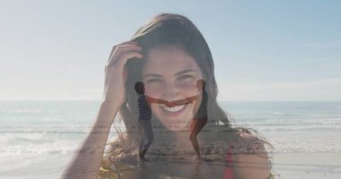 Sahilde saçlarına dokunan kırmızı tişörtlü, gülümseyen beyaz bir kadın ve sörf yapan bir çift. Eğlence, bağlantı, eğlence, açık hava, yaşam tarzı, uyum, canlı