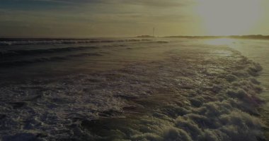 Kayan köpüklü okyanus dalgaları plaj manzarasında altın gün batımını yakalıyor, sahil manzarasında. Deniz manzarası, kıyı, ufuk, sükunet, doğal manzara, açık hava.