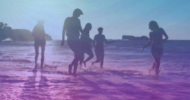 Playing group of friends wearing swimwear, splashing water at sandy shoreline, with rocky islets. Vacation, leisure, outdoors, recreation, vibrant, lifestyle, relaxation