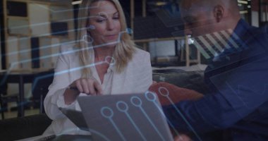 Reviewing data on laptop and tablet on office bench in blazers, colleagues using digital overlays. Corporate, teamwork, innovation, technology, collaboration, modernity, business