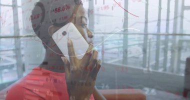 Kırmızı bluzlu bir kadın akıllı telefon tutuyor, modern salon pencerelerinden bakıyor, hisse senedi verileri üst üste biniyor. İş, finans, teknoloji, şirket, iletişim, modern, profesyonel