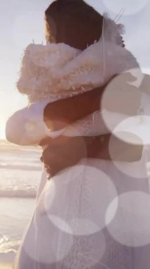 Düğünde kumsalda kucaklaşan mutlu Afrikalı Amerikalı gelin ve damadın üzerindeki ışık noktalarının animasyonu. Romantizm, aşk, tatiller ve evlilik, dijital olarak üretilen video.