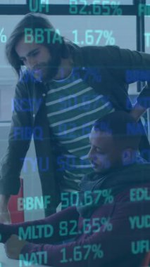 Ofiste, çeşitli takımlar ekranda finansal veri animasyonuyla işbirliği yapıyor. Takım çalışması, işbirliği, çeşitlilik, finans, ticaret, teknoloji