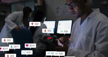 Erkek bilim adamı laboratuvarda tablet tıklayarak meslektaşlarının yazdığı gibi veri simgeleri oluşturuyor. Veri analizi, takım çalışması, işbirlikçi araştırma, bilimsel ortam, dijital arayüz, yenilik, teknoloji